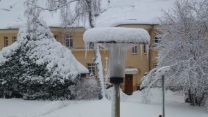 Verschneite Laterne mit Eiszapfen vor einem verschneiten Gebäude an der TU Bergakademie Freiberg