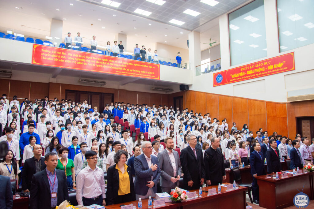 Ein Hörsaal in Vietnam voller Ehrengäste und Studierender in weißen Hemden, an den Wänden hängen gelb-rote Spruchbanner